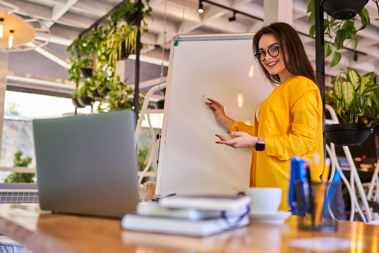 Une femme montre un tableau, un ordinateur portable est sur la table devant elle