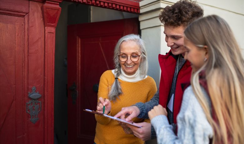 Zwei junge Menschen sprechen mit einer älteren Frau an der Haustür und lassen sie ein Formular unterschreiben.