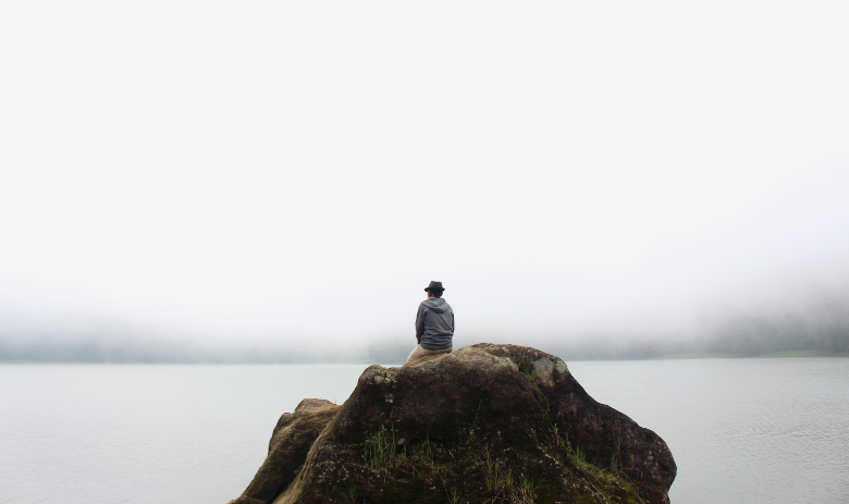 Ein Mensch sitzt auf einem Felsen in einem Nebelmeer.